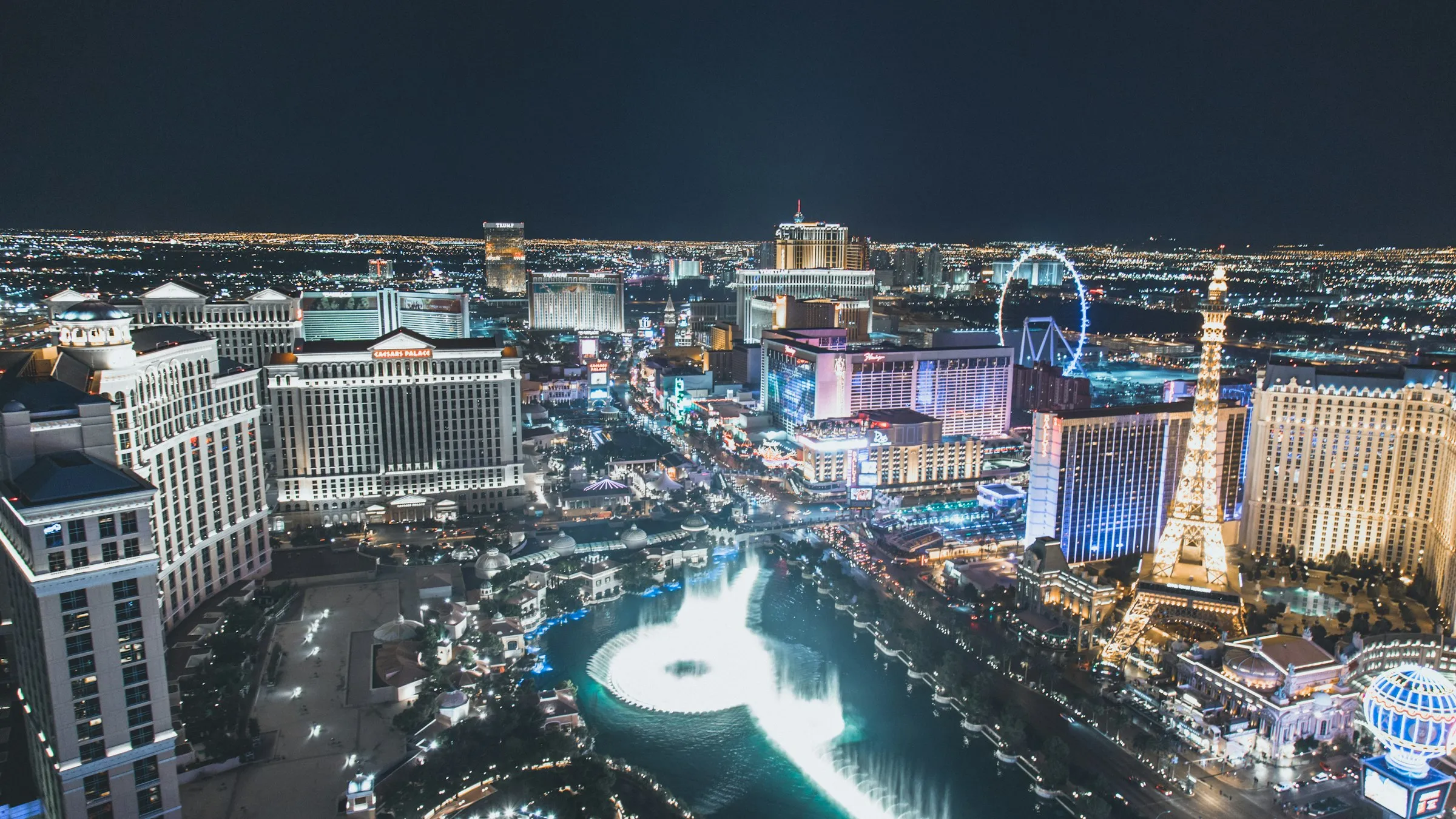 Vista do alto da Strip de Las Vegas à noite, com as fontes do Bellagio, a réplica da Torre Eiffel e a roda-gigante iluminadas