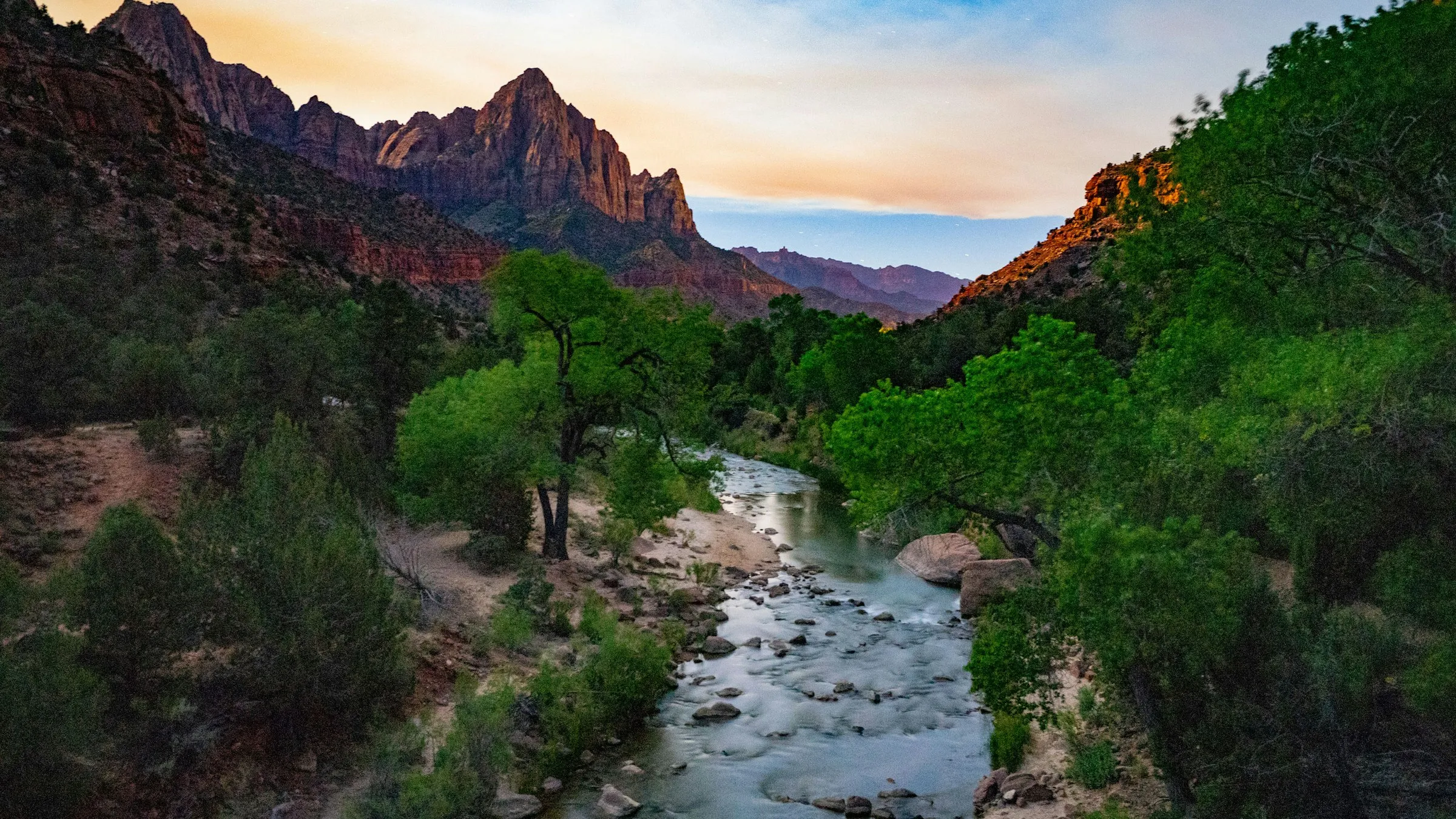 Zion: o rio Virgin corre entre árvores verdes até o pico The Watchman, iluminado ao pôr do sol