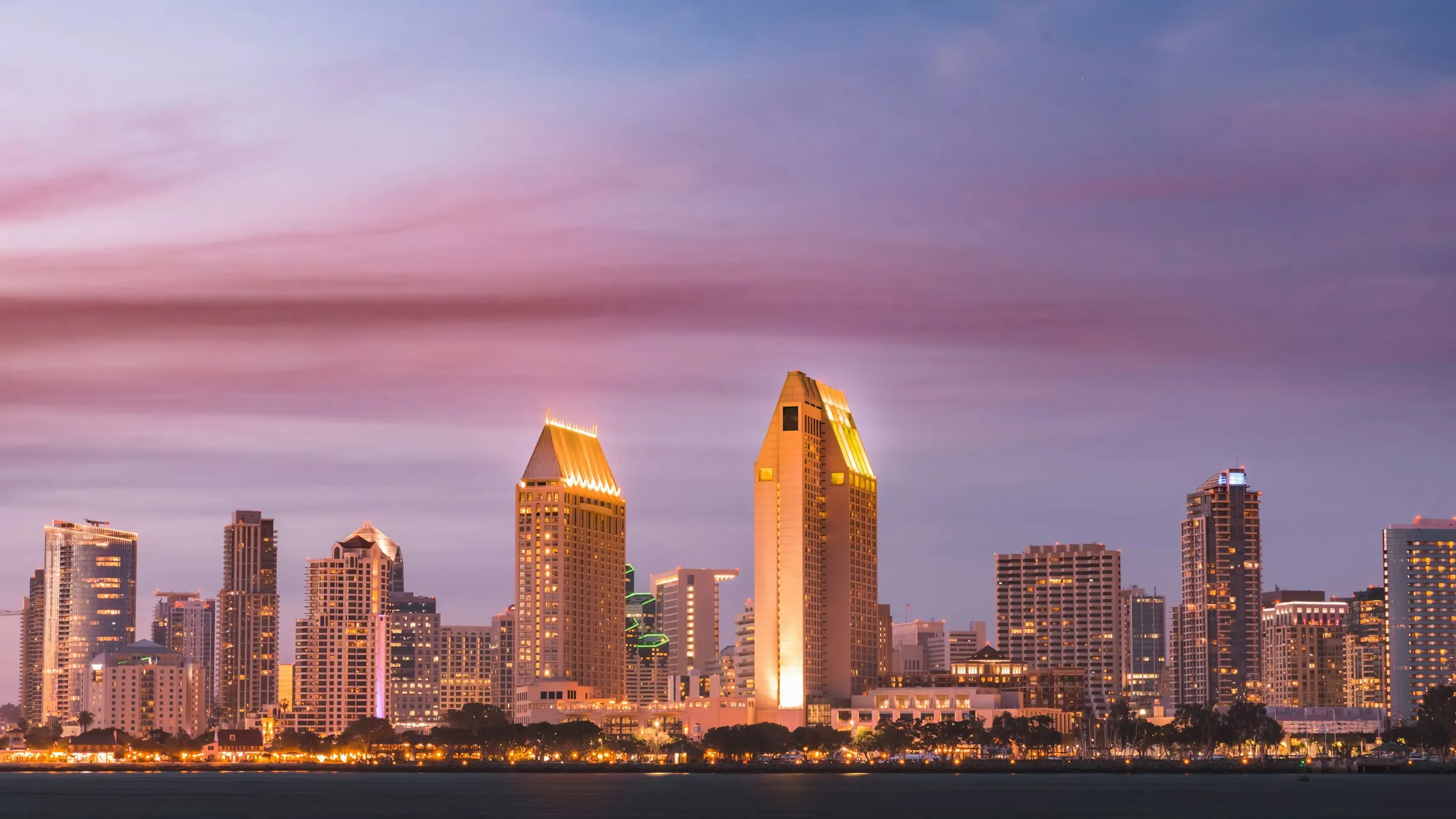 Arranha-céus do centro de San Diego iluminados ao entardecer, à beira da baía, sob céu rosado