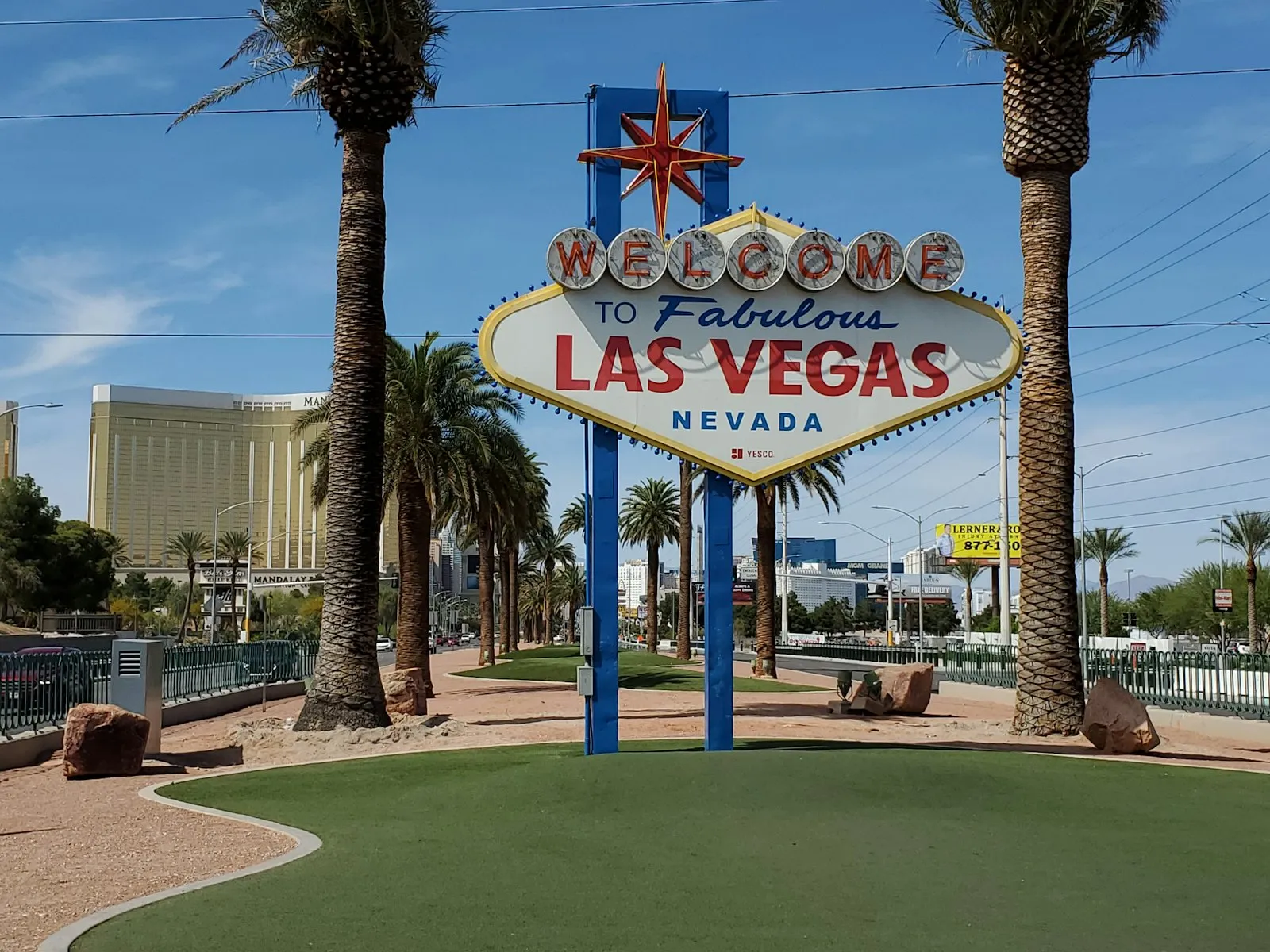 Placa "Welcome to Fabulous Las Vegas" entre palmeiras, sob céu azul, com hotéis ao fundo