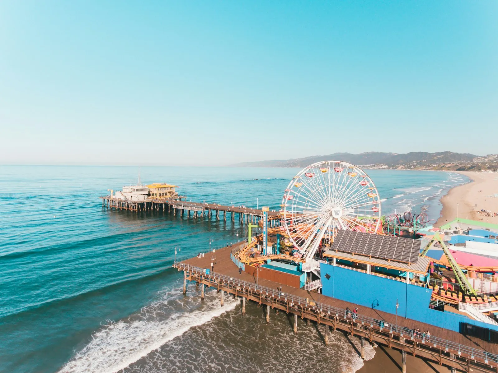 Vista aérea do píer de Santa Monica, com a roda-gigante e o mar azul-turquesa quebrando na praia
