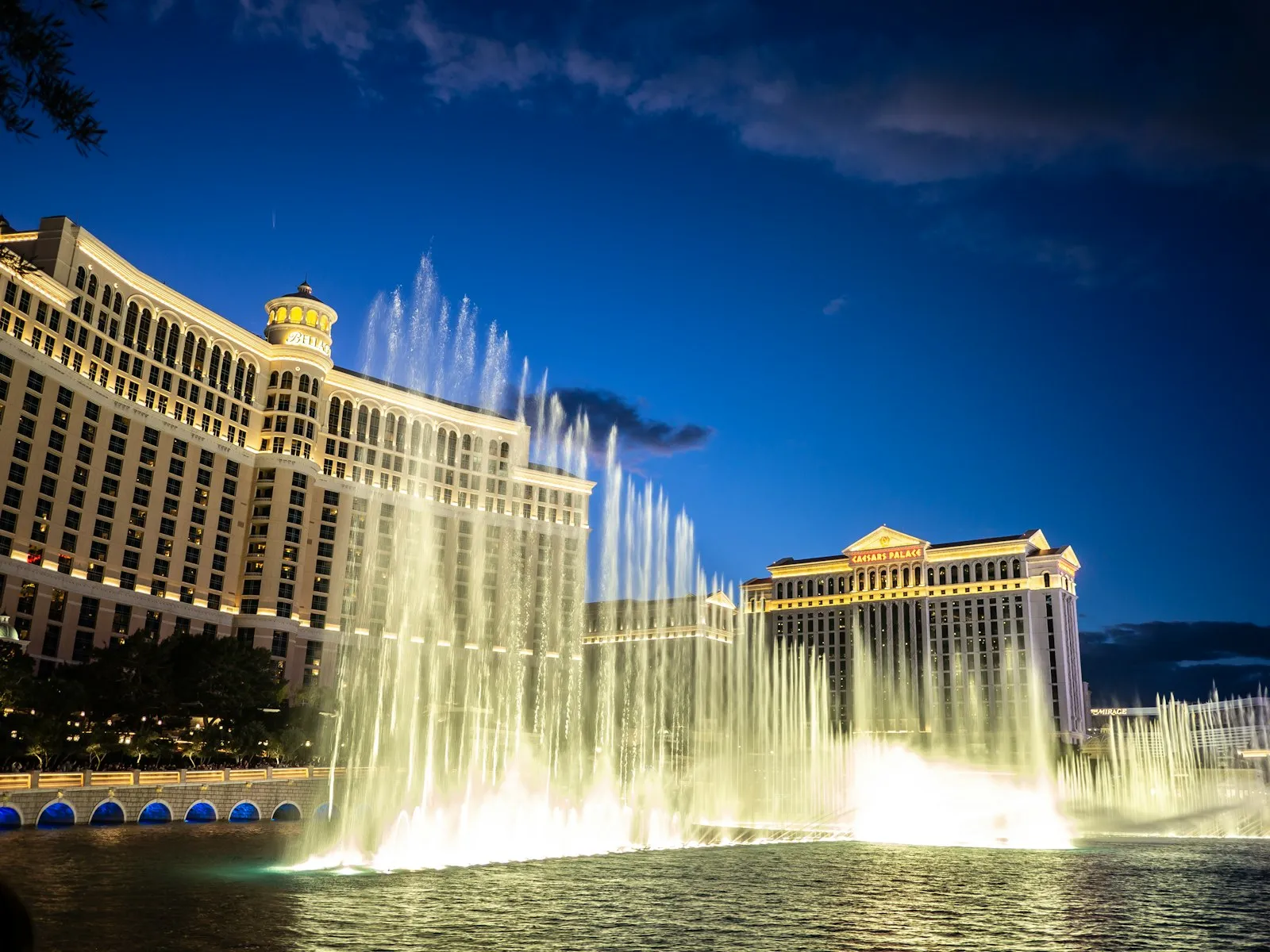 Fontes do Bellagio jorrando diante da fachada iluminada do hotel ao anoitecer, sob céu azul-escuro