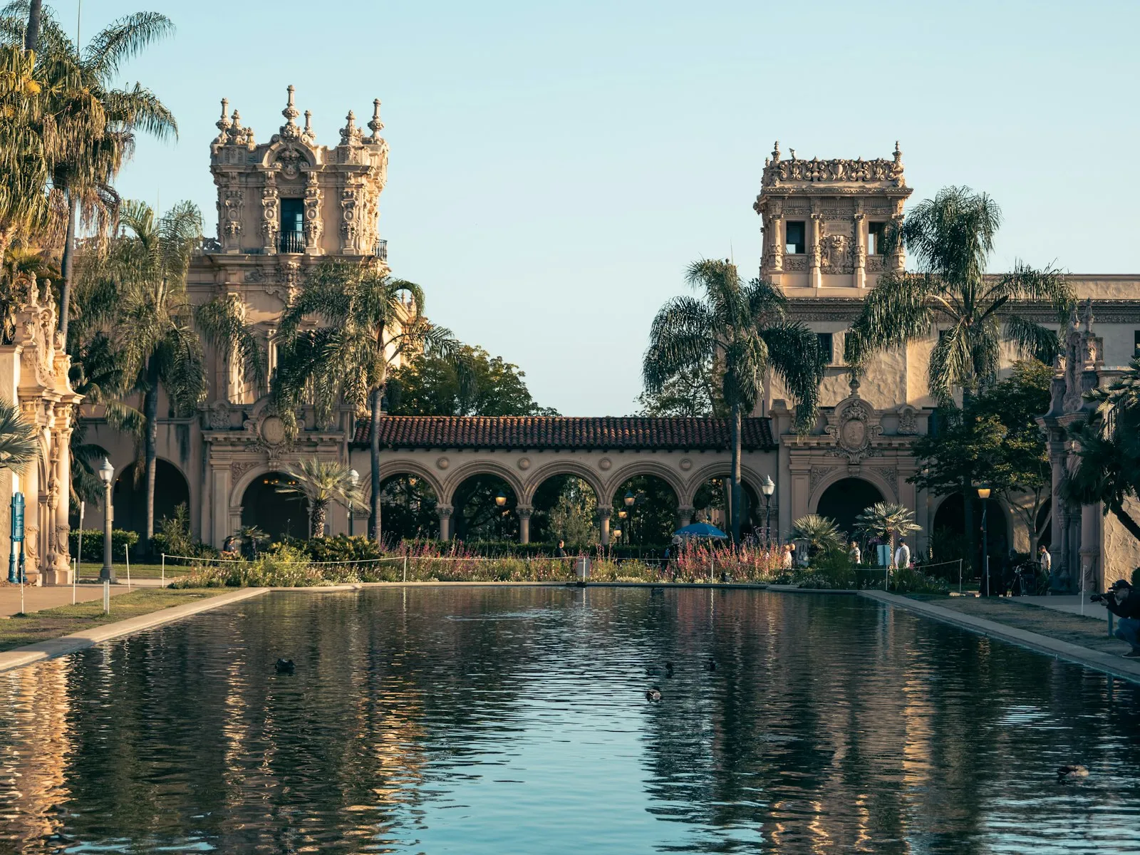 Prédios em estilo colonial espanhol do Balboa Park refletidos no espelho d'água, entre palmeiras, à luz dourada do fim de tarde