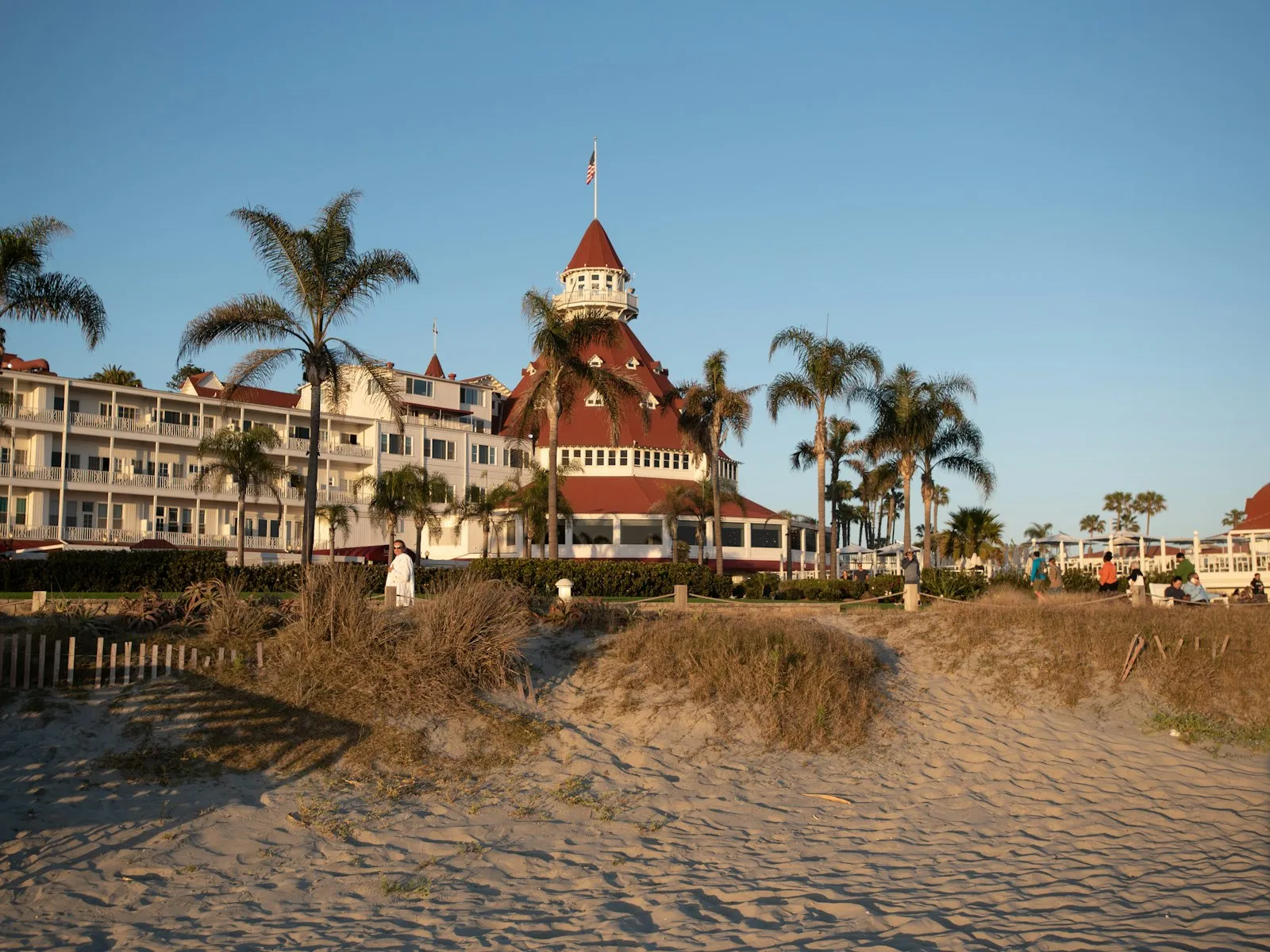Hotel del Coronado, com telhados vermelhos e palmeiras, visto da areia da praia de Coronado no fim da tarde