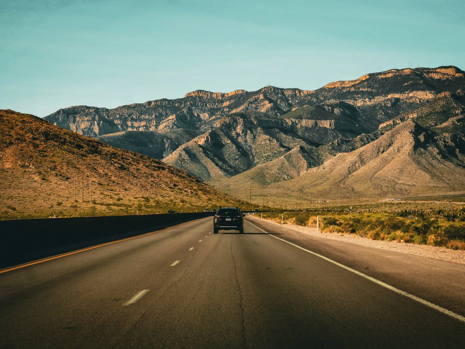 Rodovia reta no deserto de Nevada rumo às montanhas, com um carro ao longe