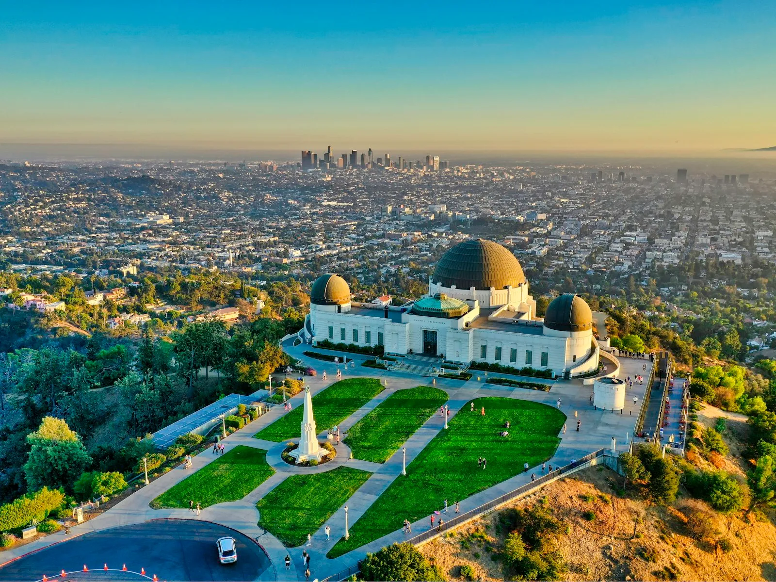 Observatório Griffith no alto da colina, com os jardins à frente e o centro de Los Angeles no horizonte, no fim da tarde